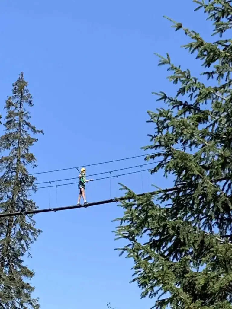 Young adventurer crossing a high rope bridge during a family climbing experience near Méribel while staying at La Petite Cachée in Les Trois Vallées.