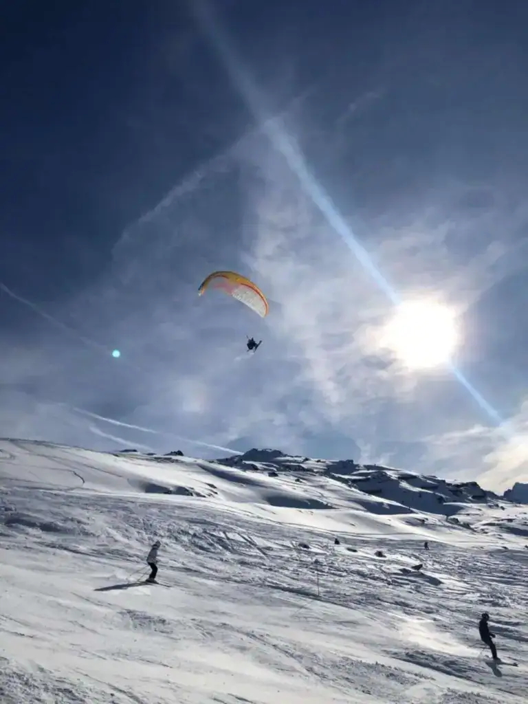 Paraglider soaring above the snowy slopes of Méribel while skiers enjoy the Three Valleys during a winter holiday near La Petite Cachée.